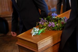 Pallbearers carrying a wooden casket with purple flowers resting on top