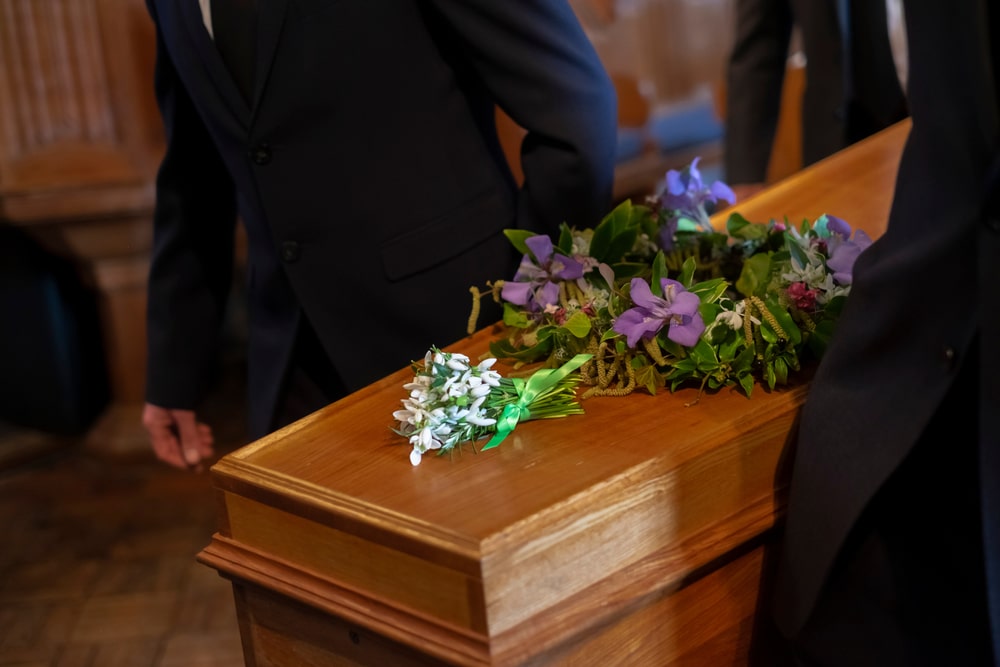 Pallbearers carrying a wooden casket with purple flowers resting on top