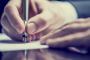 Person holding a pen and writing a message on a notecard