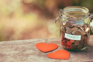 glass jar full of change marked "charity" sitting on a wooden table next to two paper hearts