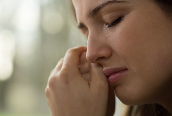 woman crying with her hands clasped by her face