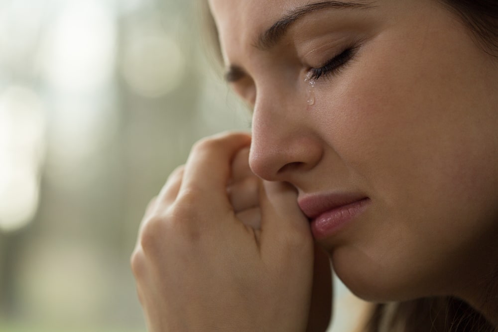 woman crying with her hands clasped by her face