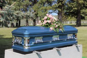 Blue metal casket with pink flower spraying, waiting for burial