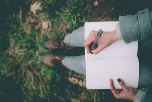 Person sitting outside, writing on a pad of paper