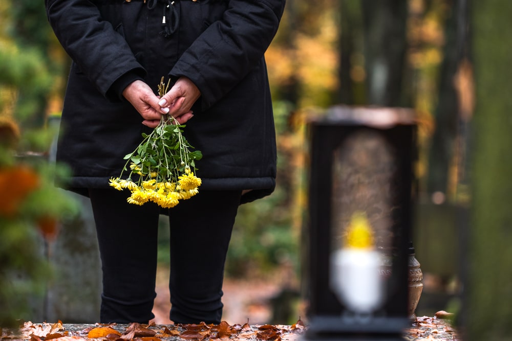 Woman wearing black and holding yellow flowers as she visits a loved one's grave