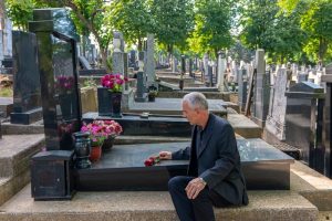Mature man sitting next to a loved one's gravesite, leaving a flower of remembrance