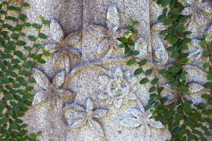 headstone carved with flowers with plants growing over it