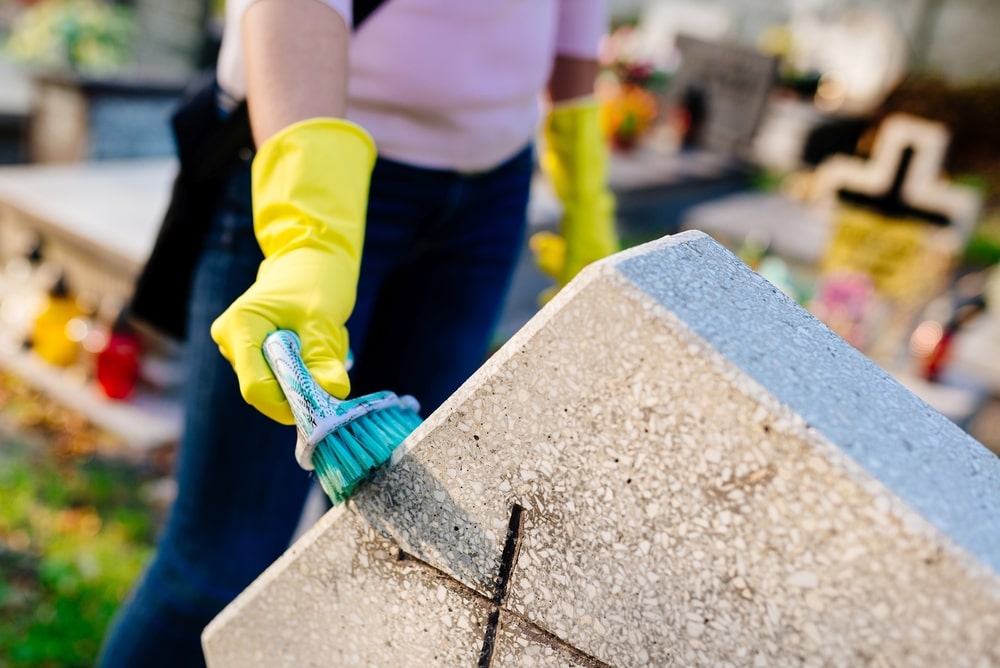 woman with cleaning gloves using a brush to clean a headstone