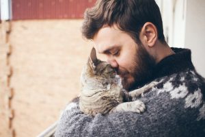 Man in dark-colored sweater hugs gray cat