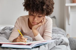 Young woman laying on bed, writing in journal