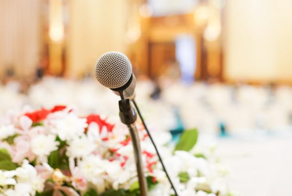 Microphone ready for eulogy; white and red flowers and chairs in the background