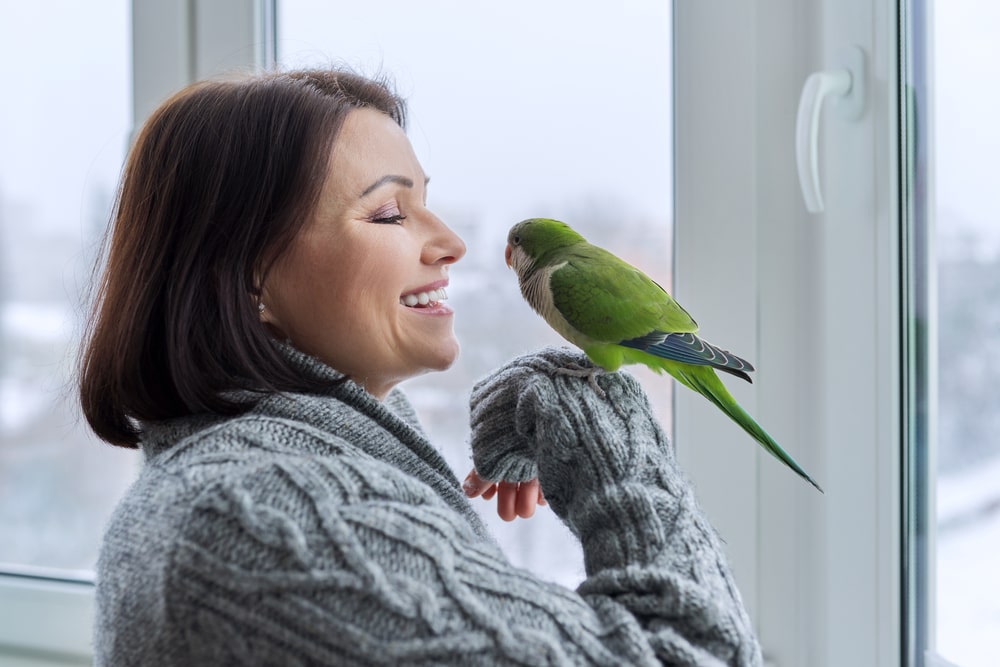 Woman with a gray fuzzy sweater holding a small green bird and smiling
