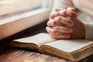 Open Bible with unidentified person resting clasped hands on top