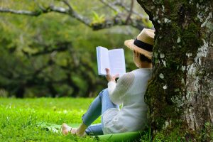 Woman sitting outside alone, leaning against a tree and reading a book