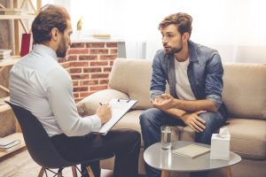 Young man sitting on a couch, speaking with a grief counselor who is taking notes