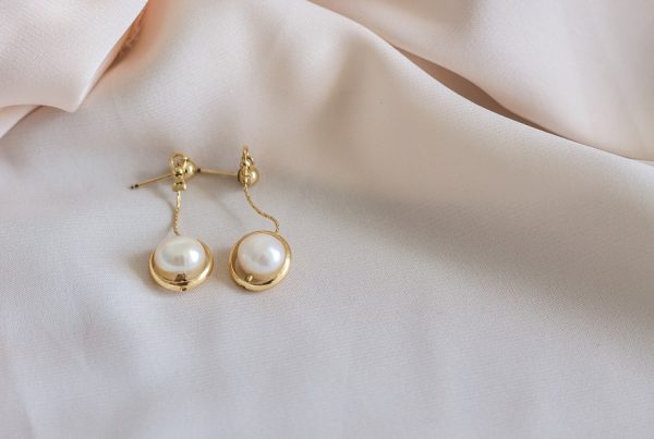 Gold pearl earrings resting on white fabric