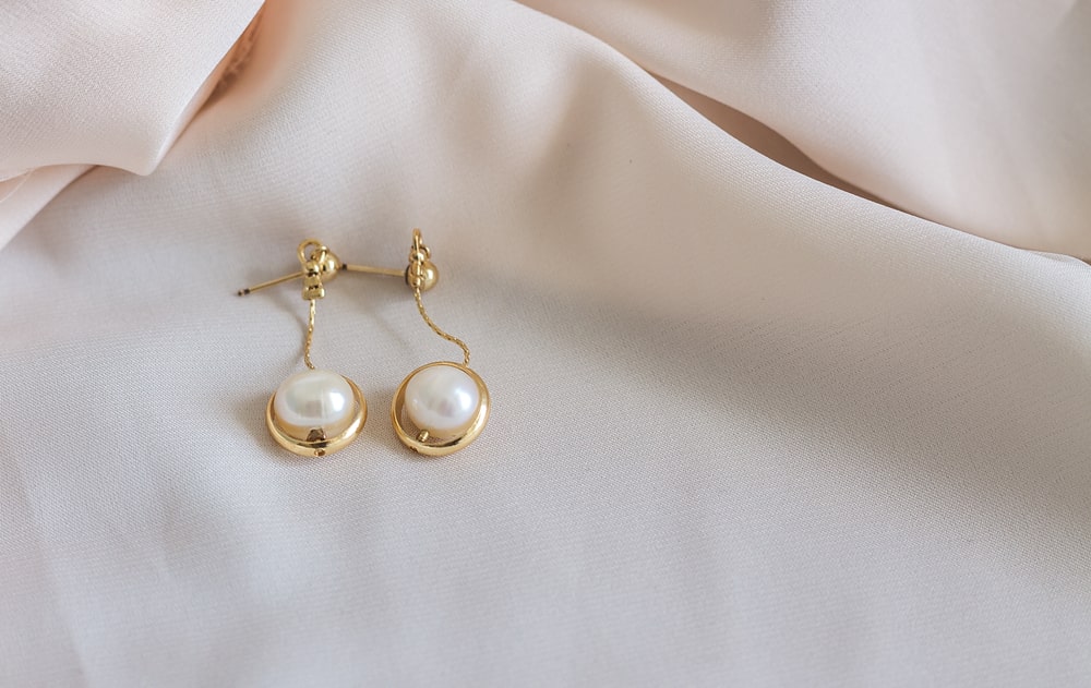Gold pearl earrings resting on white fabric