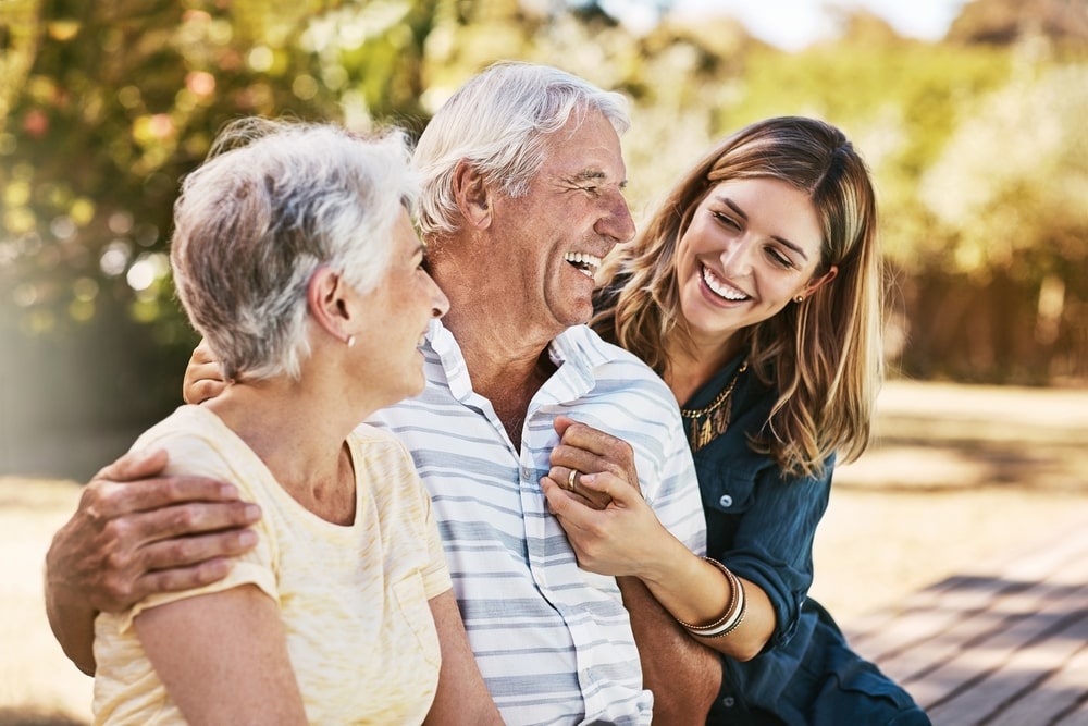 young woman sitting on a bench, smiling with her elderly parents