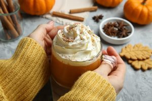 Woman in yellow sweater holding mug of pumpkin spice latte