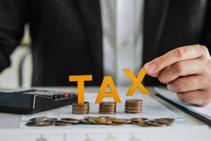 Man in suit holding the "X" on the word "TAX" spelled out