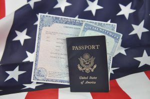 Image of American passport, birth certificate, and social security card set against backdrop of American flag