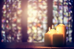 Three white remembrance candles against the backdrop of a church's stained glass window