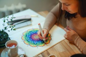 Woman sitting at table at home with a cup of tea, coloring a mandala picture