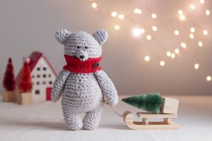 Knit white bear with red scarf and pulling sled with Christmas tree