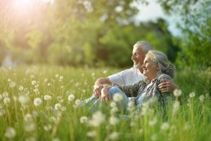 Older happy couple sitting in a green field of dandelions