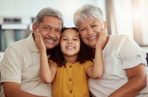 small girl in a yellow shirt in between her grandparents placing her hands on their cheeks