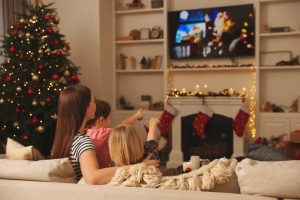 Mother sitting on couch, watching a Christmas movie with her young children