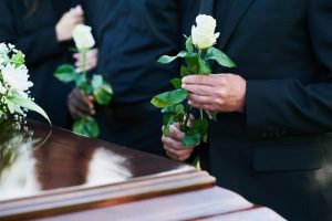 People standing next to a casket, holding white flowers