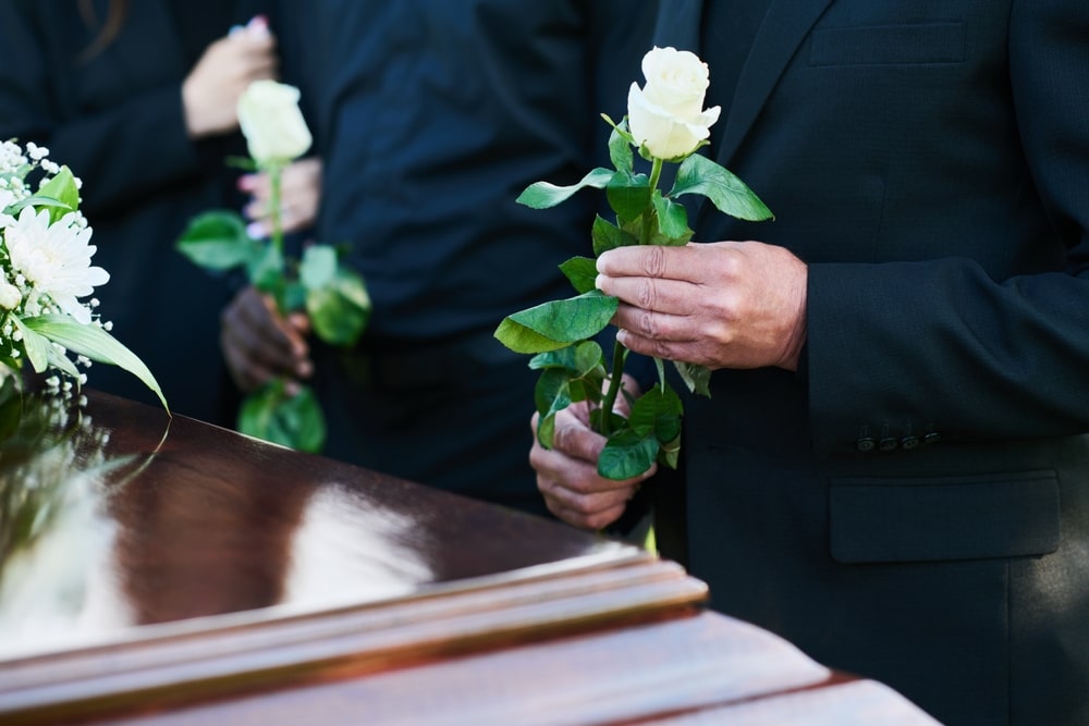 People standing next to a casket, holding white flowers