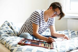 Young man sitting on his bed, coloring in a book