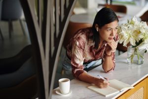 Young woman looking out a window and writing in a gratitude journal