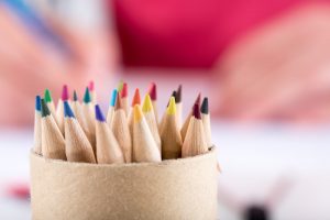 Person coloring in the background with container of colored pencils in the foreground