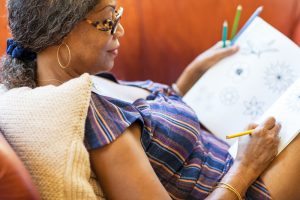 Middle-aged woman reclining comfortably on couch as she colors in a coloring book