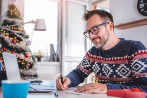 Man in sweater sitting at table, writing a letter and softly smiling