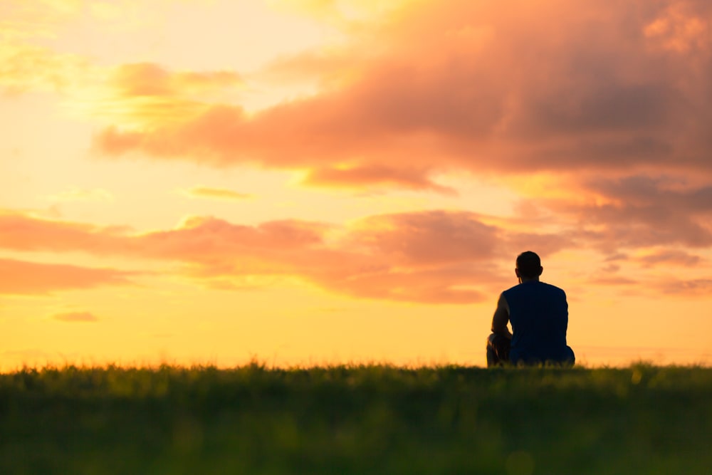 person sitting outside on the grass watching a sunset