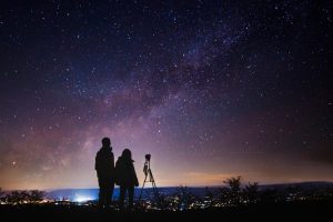 Man and woman sitting in a secluded space with a telescope, looking at the night sky
