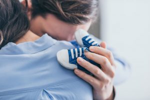 two people hugging, one holding small baby shoes