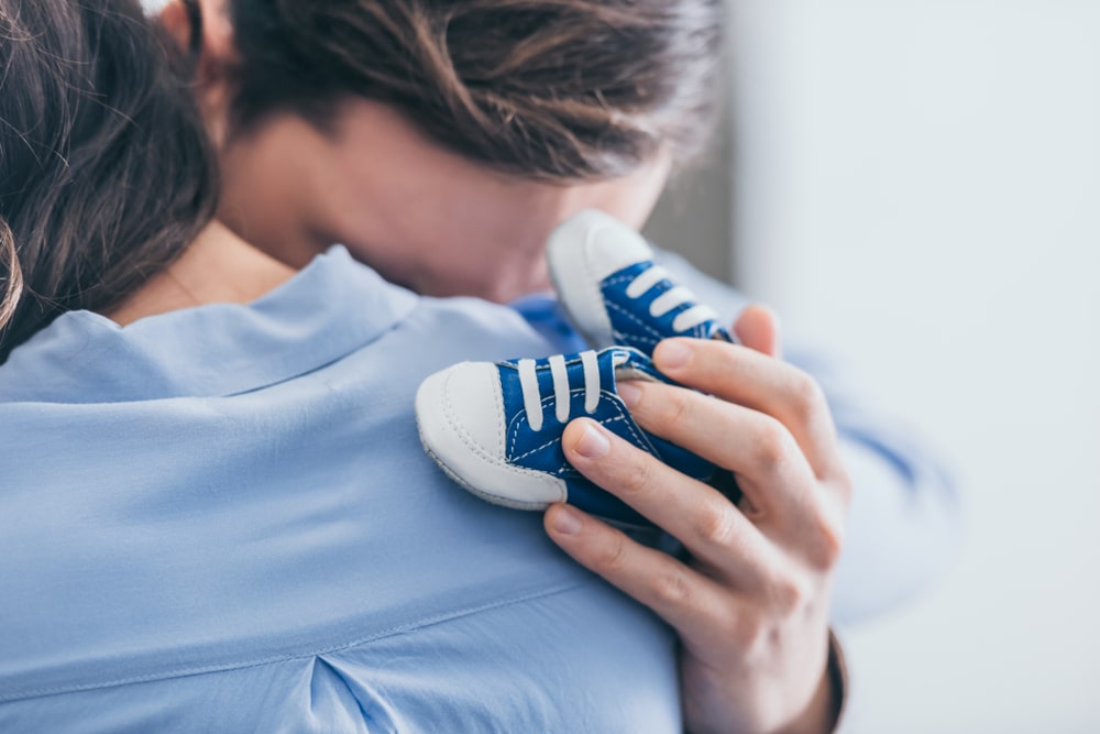 two people hugging, one holding small baby shoes
