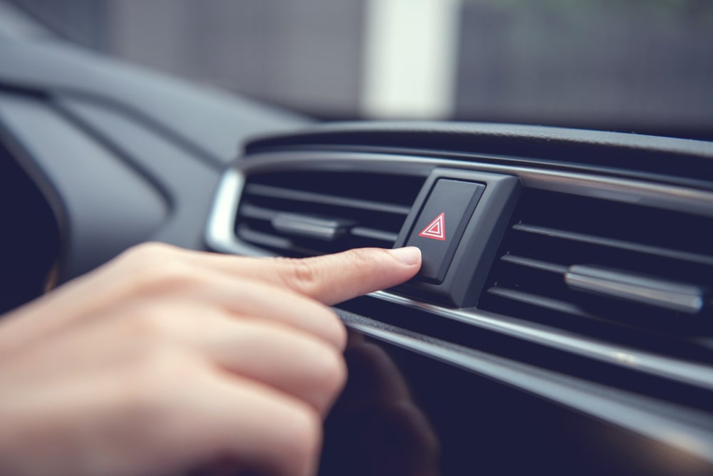 person's hand pressing the hazard light button in a car