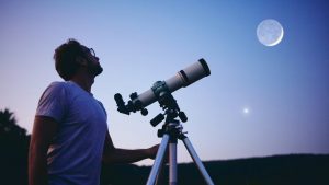 Man looking up at the darkening sky with telescope beside him