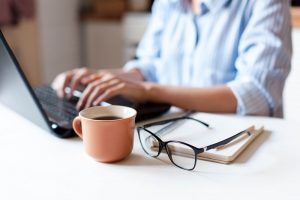 Person sitting at table at home with laptop and cup of coffee