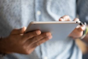 Man in button-down shirt holding a tablet, focus on tablet