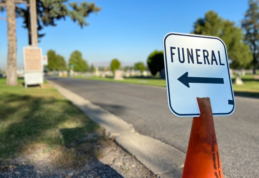 sign by a road on an orange cone that says funeral with an arrow pointing to the left