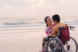woman smiling at a boy in a wheelchair on a beach