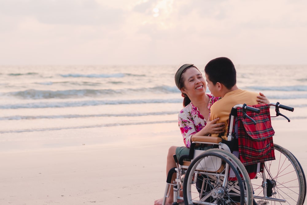 woman smiling at a boy in a wheelchair on a beach