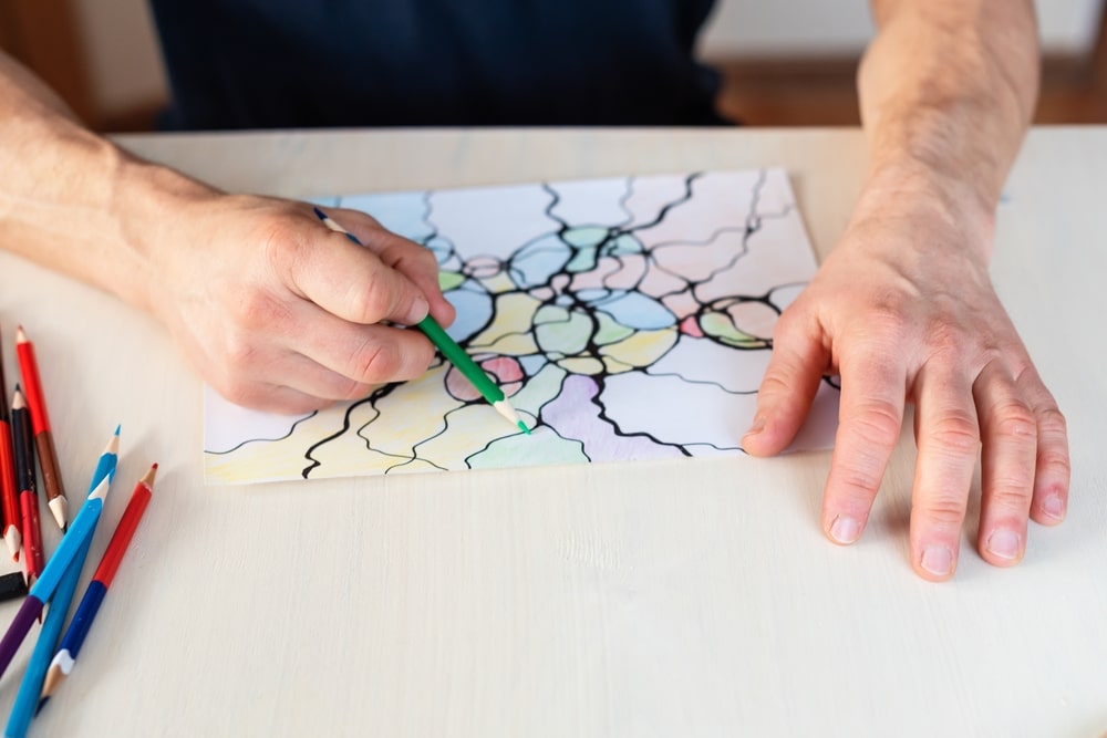 man coloring a coloring page with black cracks drawn on it